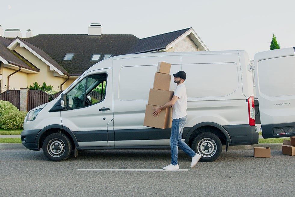 a man carrying boxes walking by a van